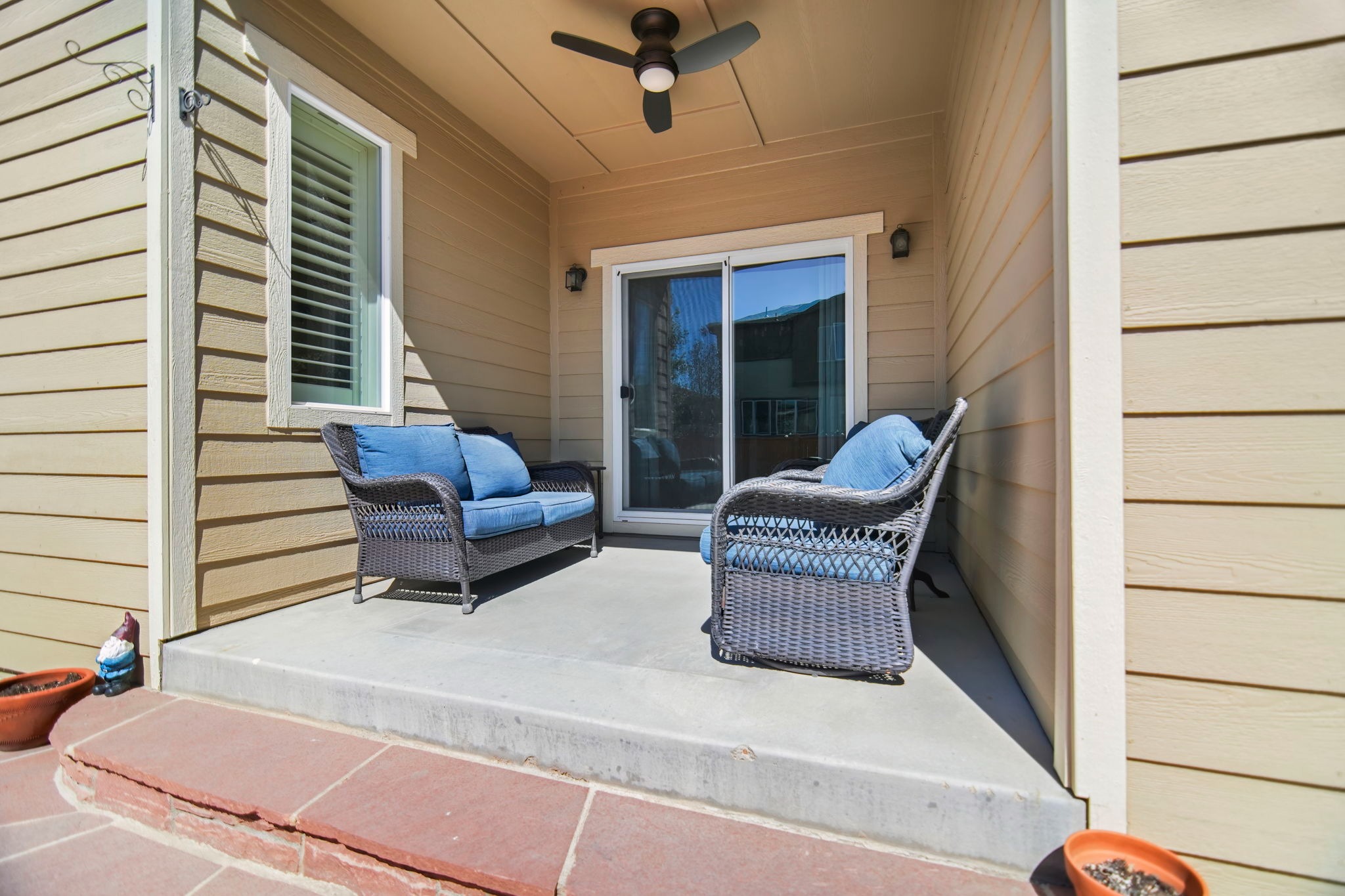  Step outside to the backyard, where a large concrete patio with outdoor furniture, planters, and a ceiling fan under the covered area offers the perfect space.